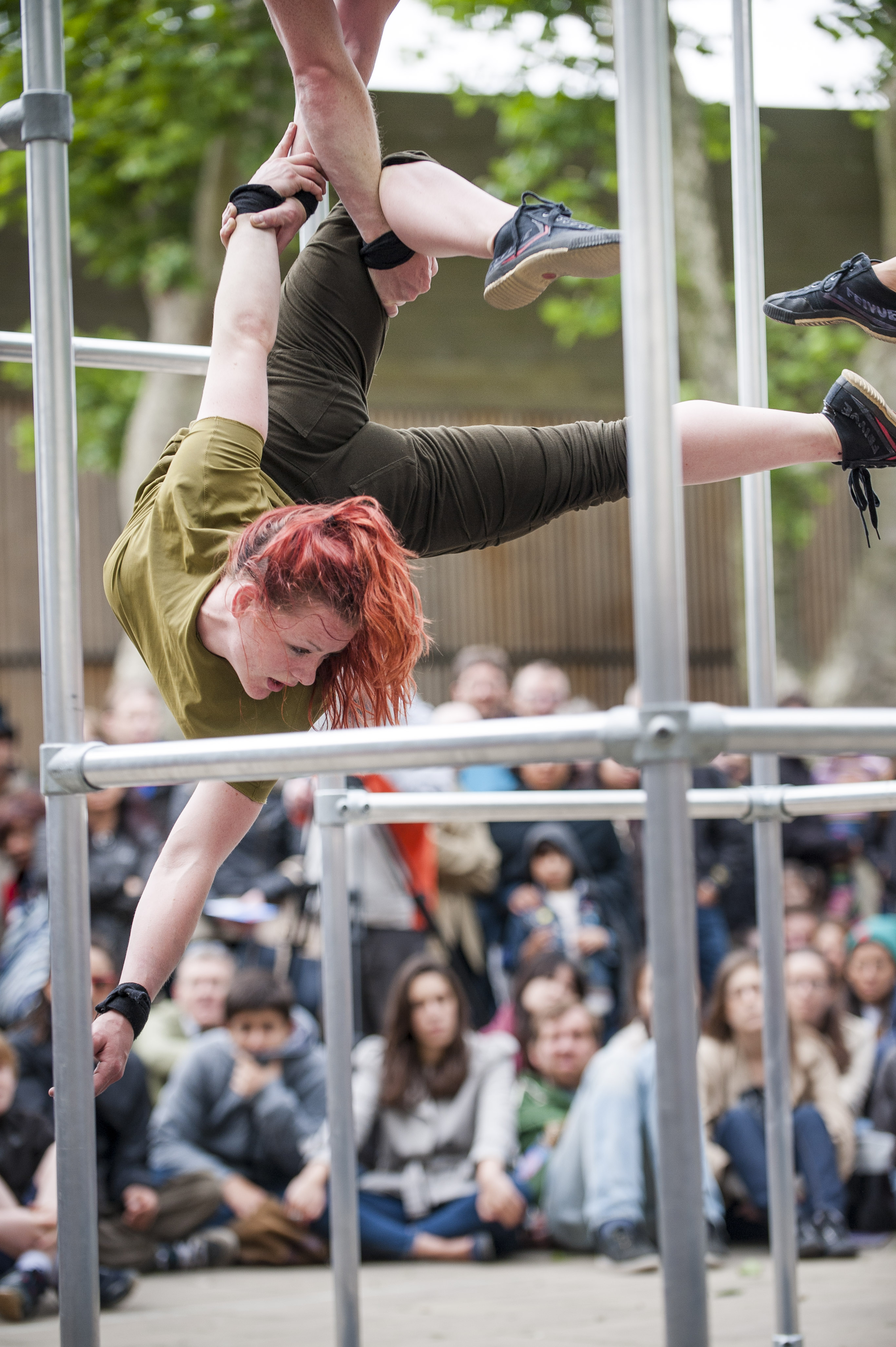 Dancer hangs suspended in the air in-between the bars of the cage