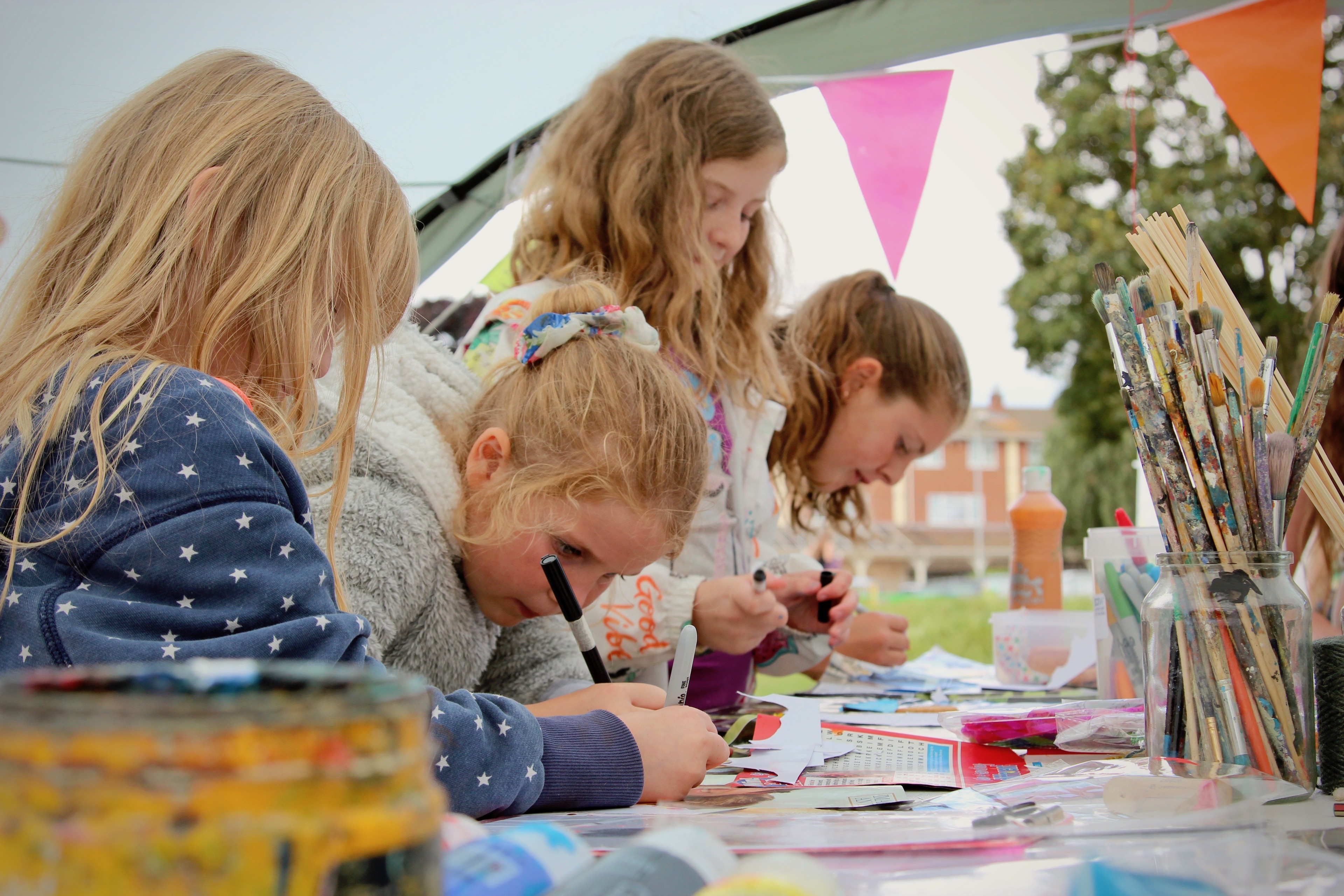 Image of 4 girls doing arts & crafts in an outdoor tent with bunting hanging in the background