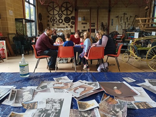 Banners of Chard workshop - images laid out on the table with a group of adults and children in a museum workshop huddled around a table